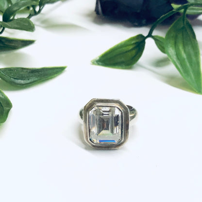 Large vintage silver cocktail statement ring with emerald cut clear stone sitting on white surface with green leaves in background