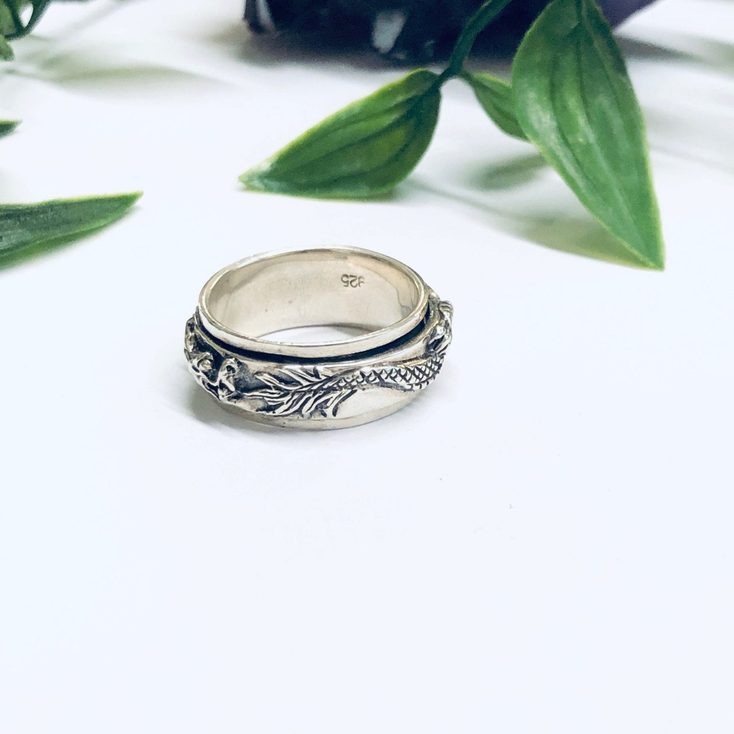 Vintage silver dragon spinner meditation ring on white surface with leaves in background