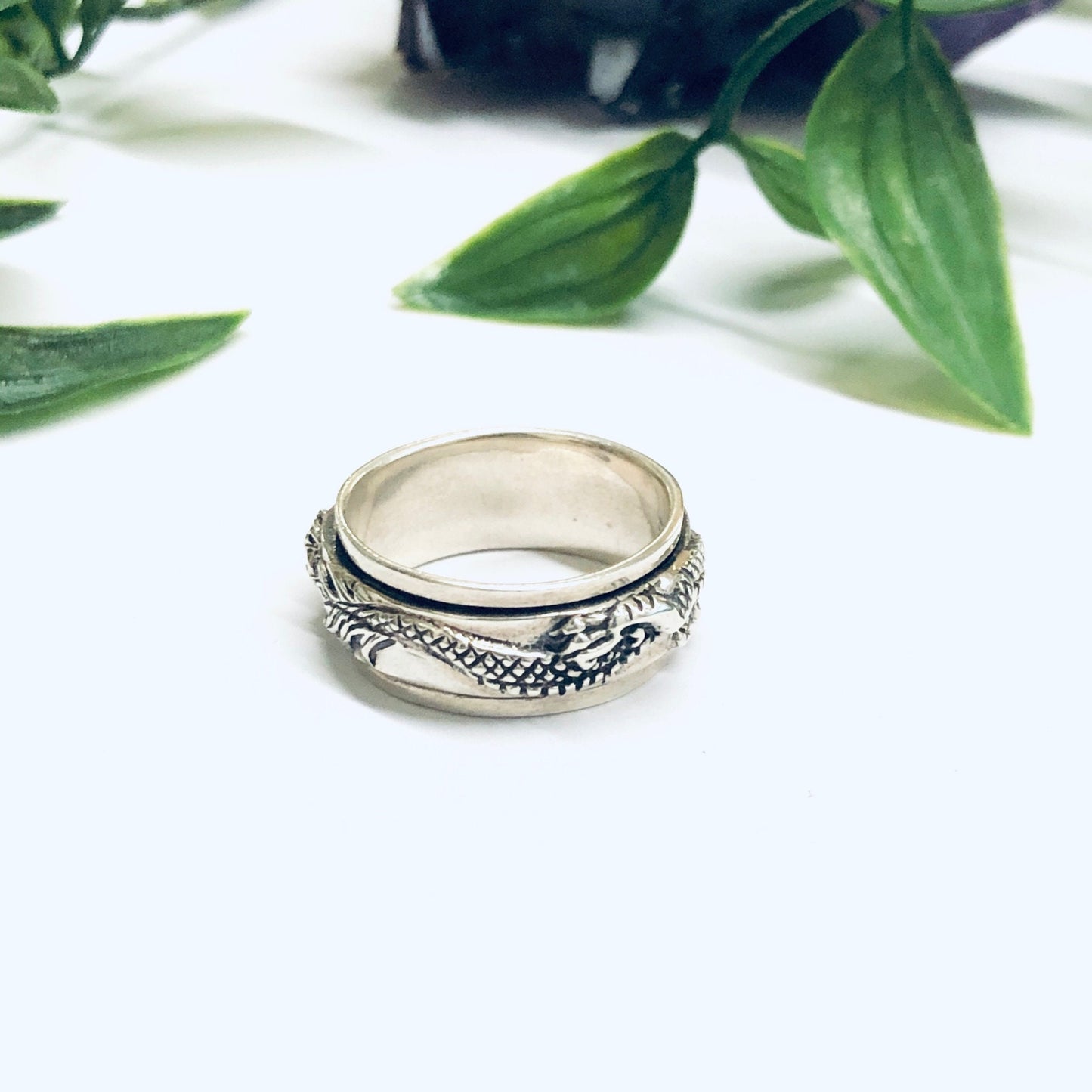 Vintage silver dragon spinner meditation ring on white background with green leaves