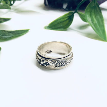 Vintage silver dragon spinner meditation ring on white surface with green leaves in background