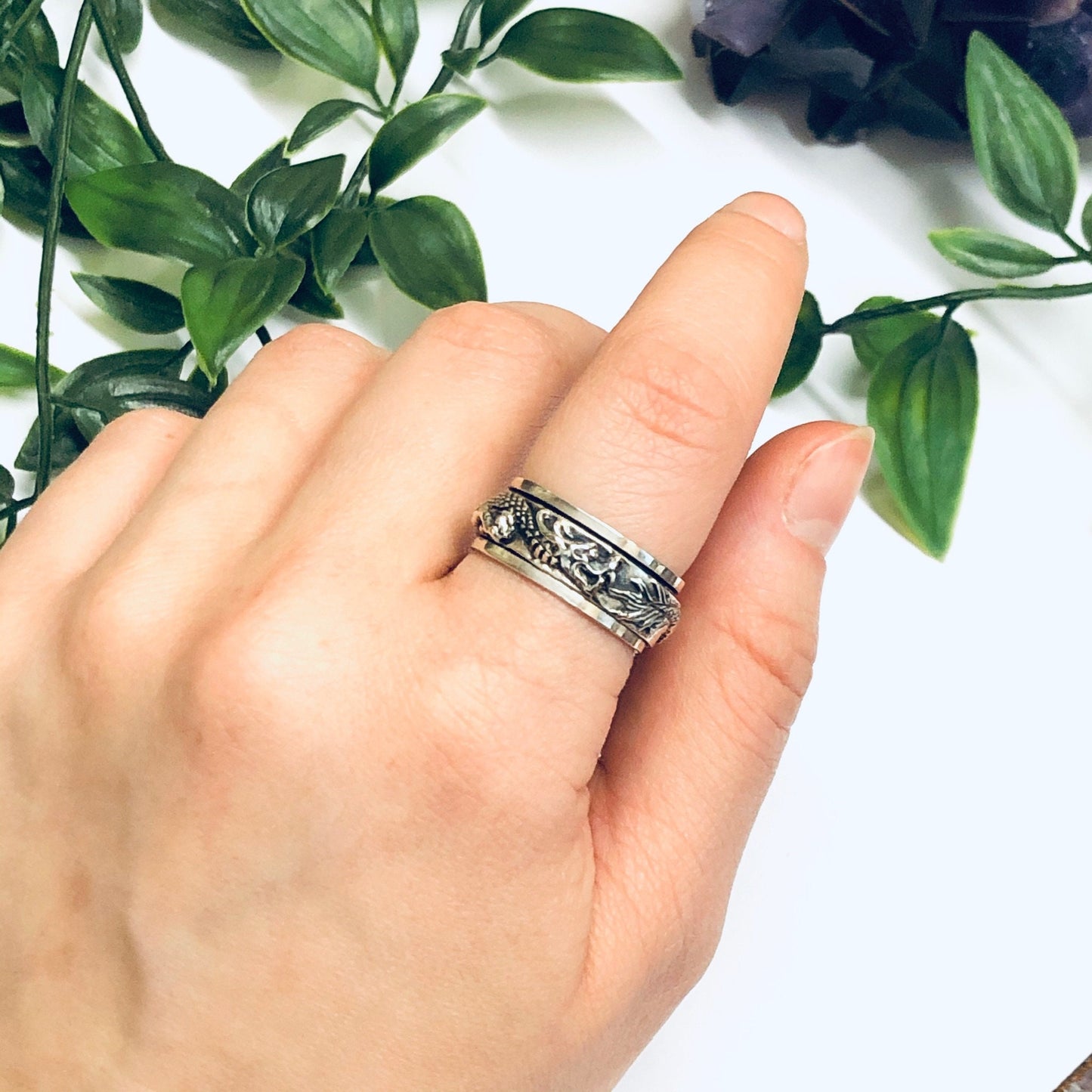 Vintage silver dragon spinner meditation ring on finger with greenery in background