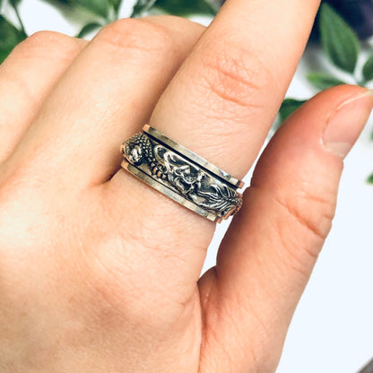 Vintage silver dragon spinner meditation ring worn on finger, surrounded by green leaves