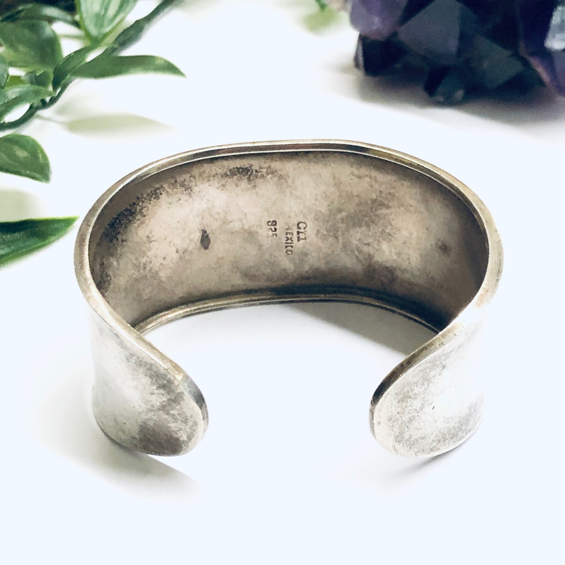 Vintage silver cuff bracelet with an onyx stone inlay, featuring a wide curved design. The tarnished, aged silver provides an antique look to this statement jewelry piece.