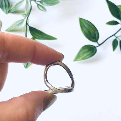 Vintage silver cut-out ring with minimalist style and abstract design, held against a white background with green leaves in the corner