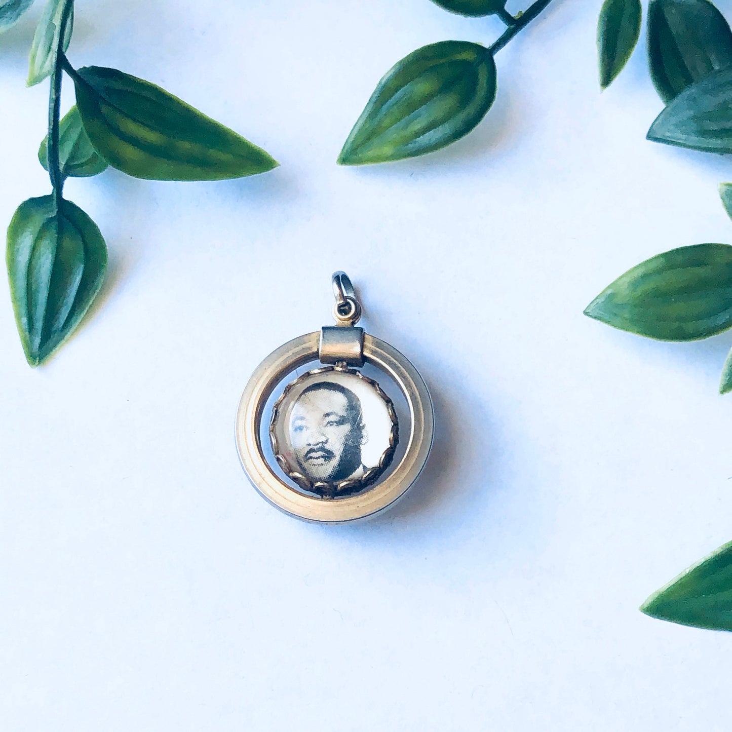 Vintage gold-toned Martin Luther King Jr. spinner pendant with 'I Have a Dream' inscription on a white background surrounded by green leaves, unique memorial jewelry.