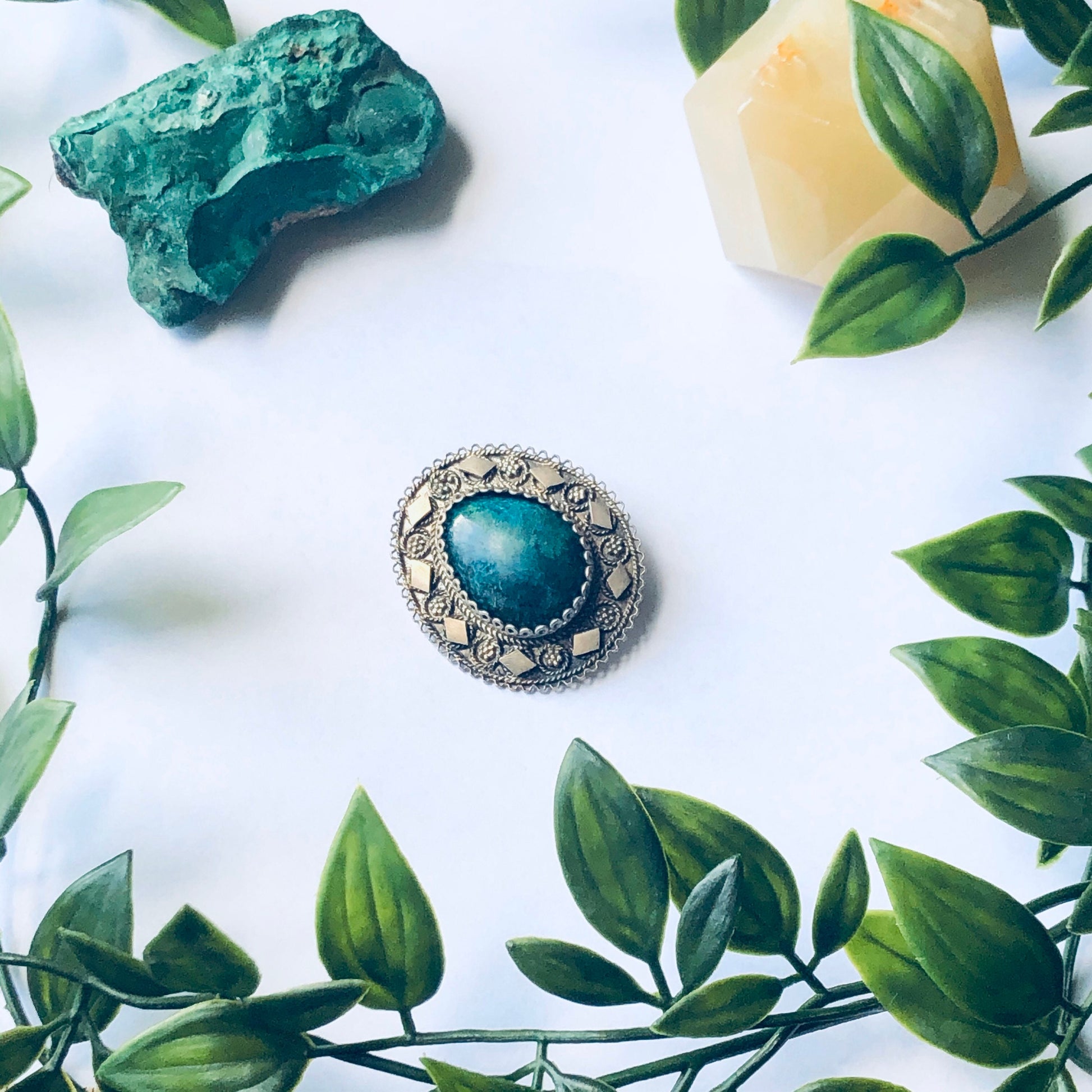 Vintage silver brooch and pendant with green stone, surrounded by leaves, on white background