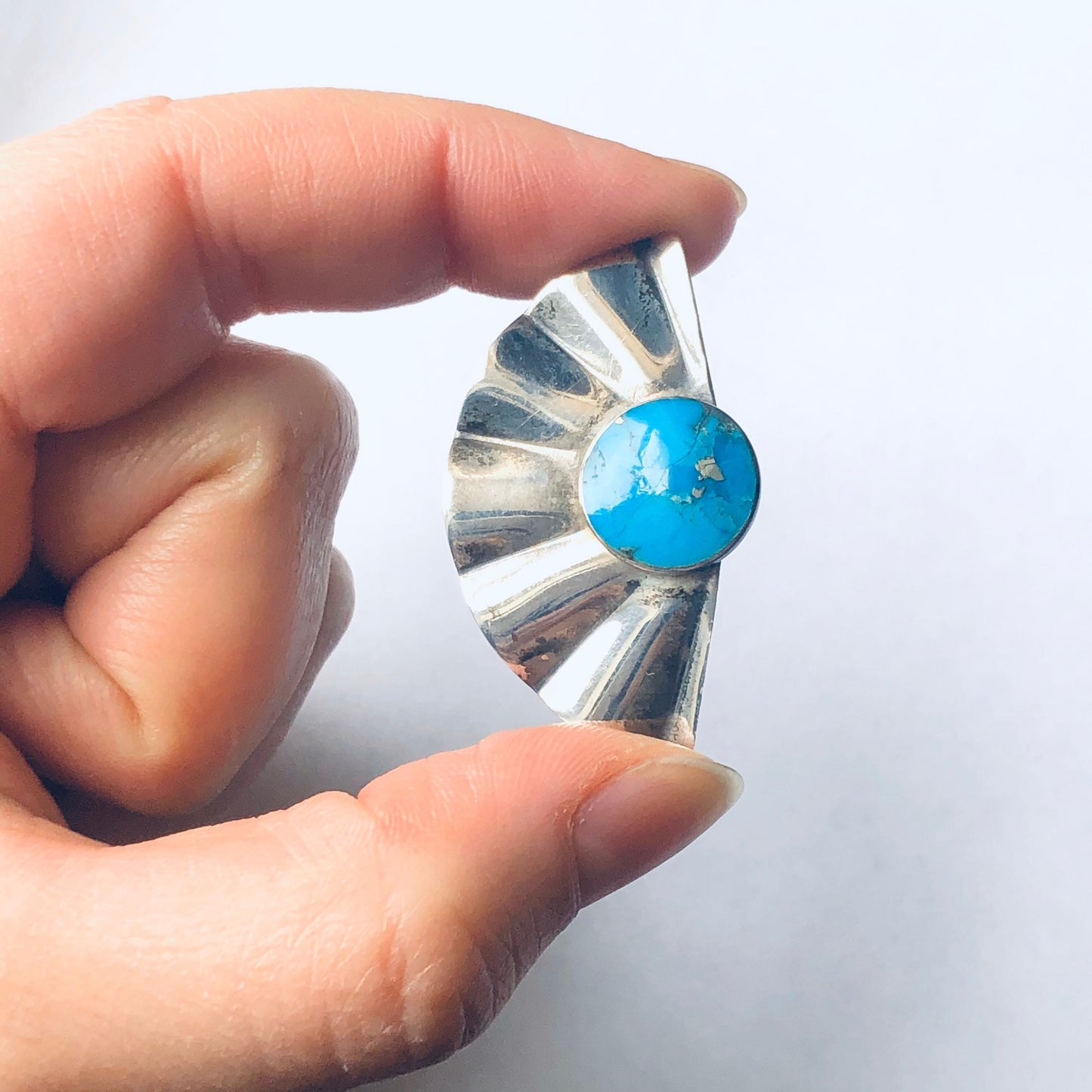 Vintage silver fan-shaped earrings with bright blue turquoise stone held in hand against white background