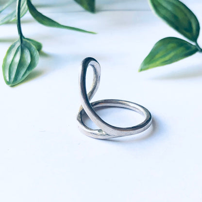 Vintage silver cut out ring with minimalist abstract design displayed against a white background with green leaves