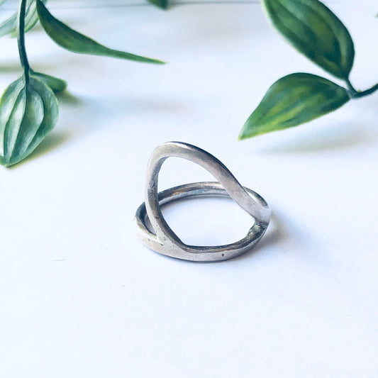 Vintage silver ring with abstract cut out design on white background with green leaves