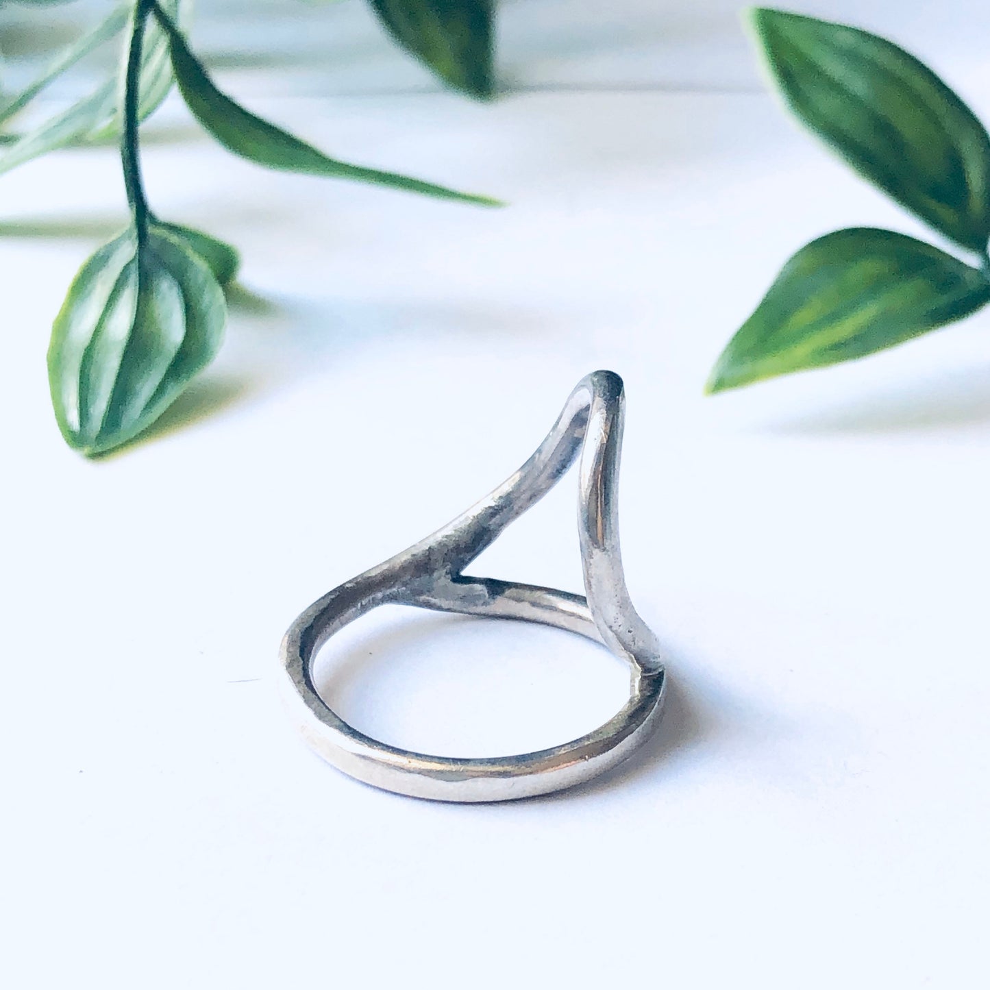 Vintage silver cut out ring with minimalist abstract design displayed on white background with green leaves in the background.