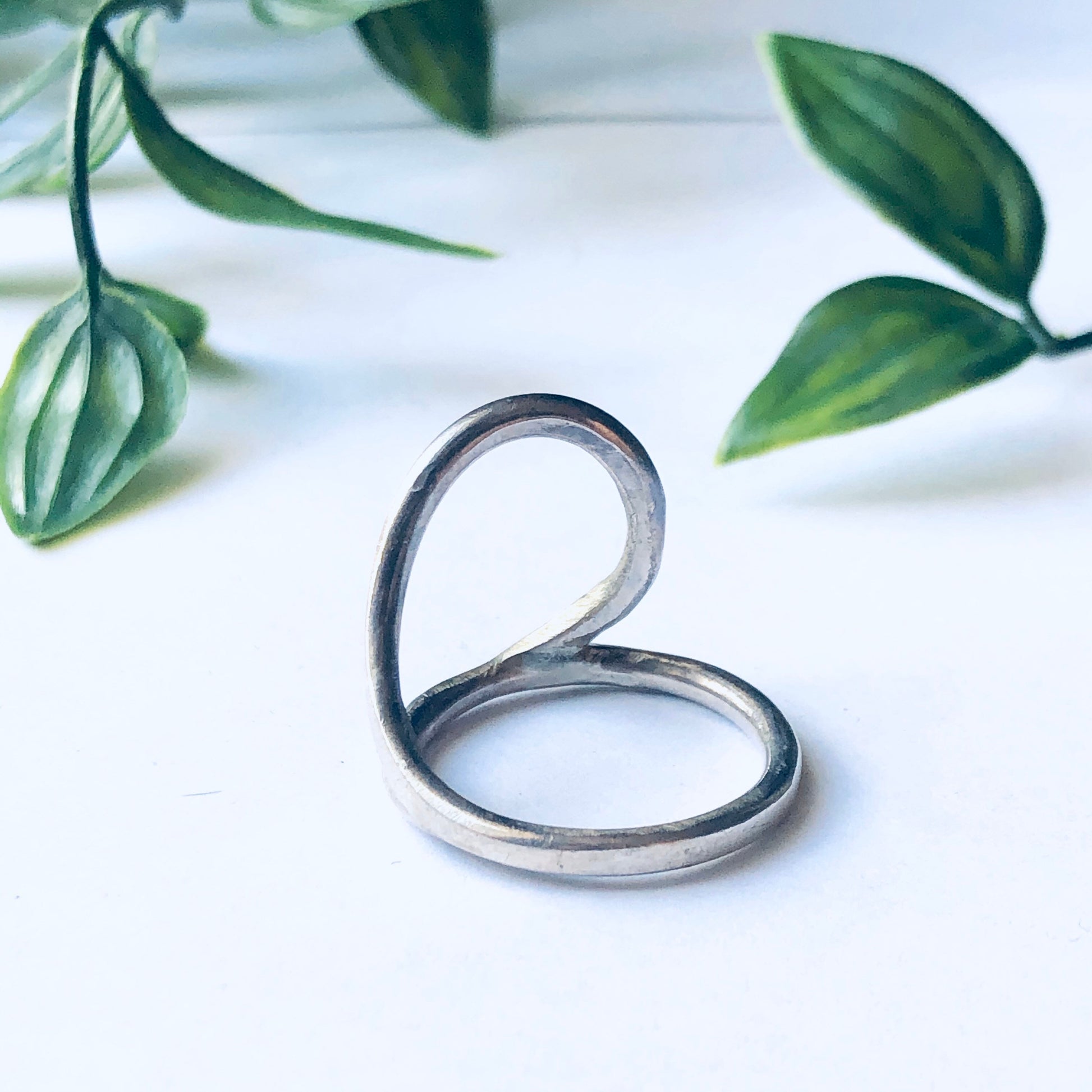 Vintage silver cut out ring with minimalist style and abstract design, displayed beside green leaves for a natural aesthetic.