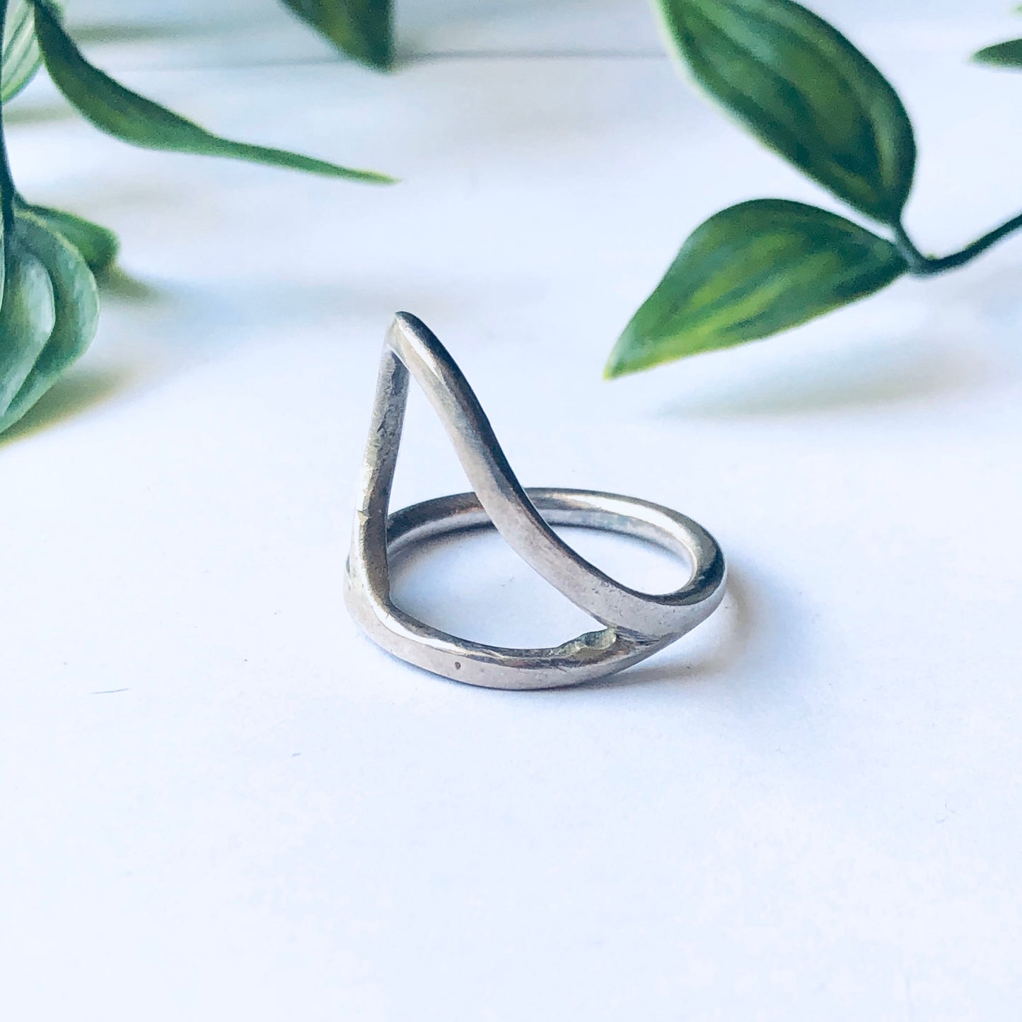 Vintage silver cut out ring with minimalist style and abstract design displayed against a white background with green leaves.