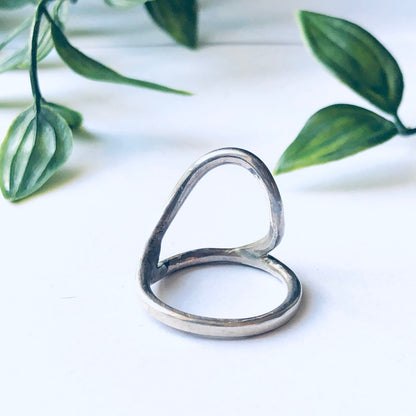 Vintage silver cut out ring with minimalist abstract design displayed on white background with green leaves in the background