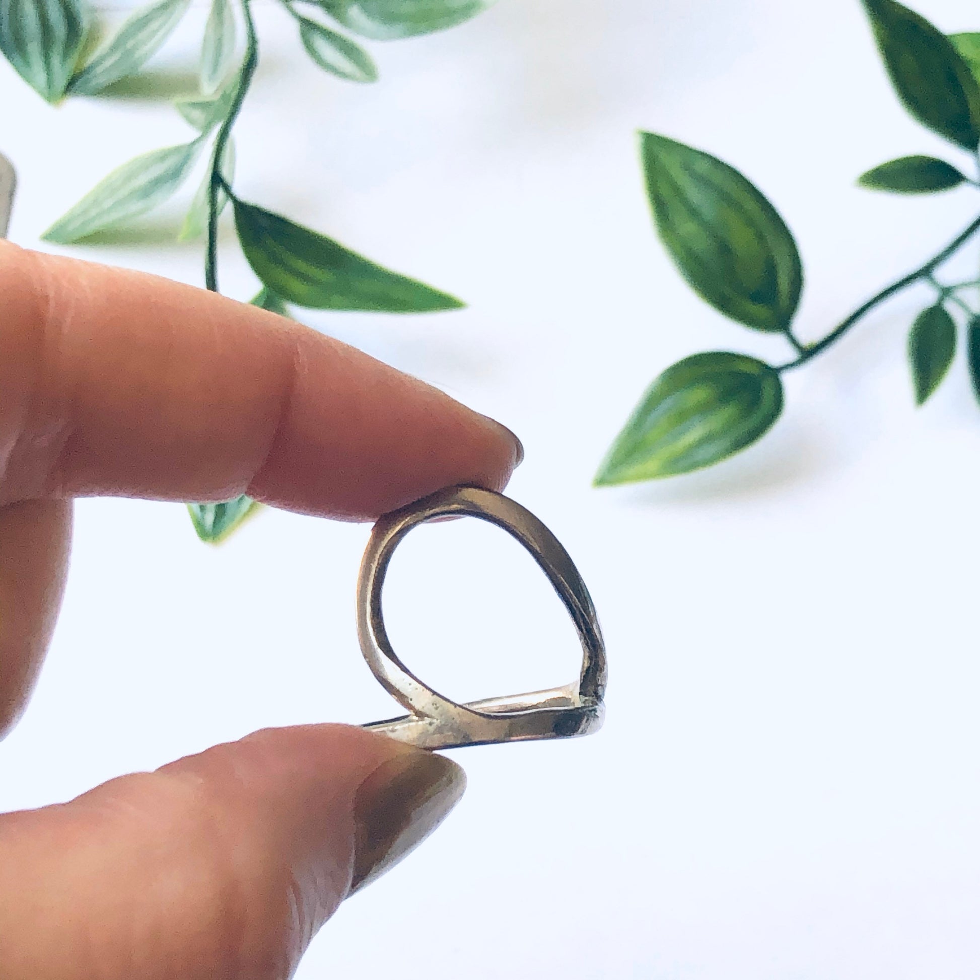 Vintage silver cut out ring with minimalist style and abstract design, held between fingers against a white background with green leaves.