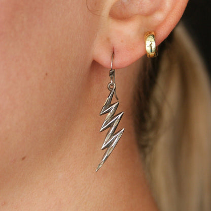 Vintage sterling silver lightning bolt dangle earrings with carved details on a woman's ear