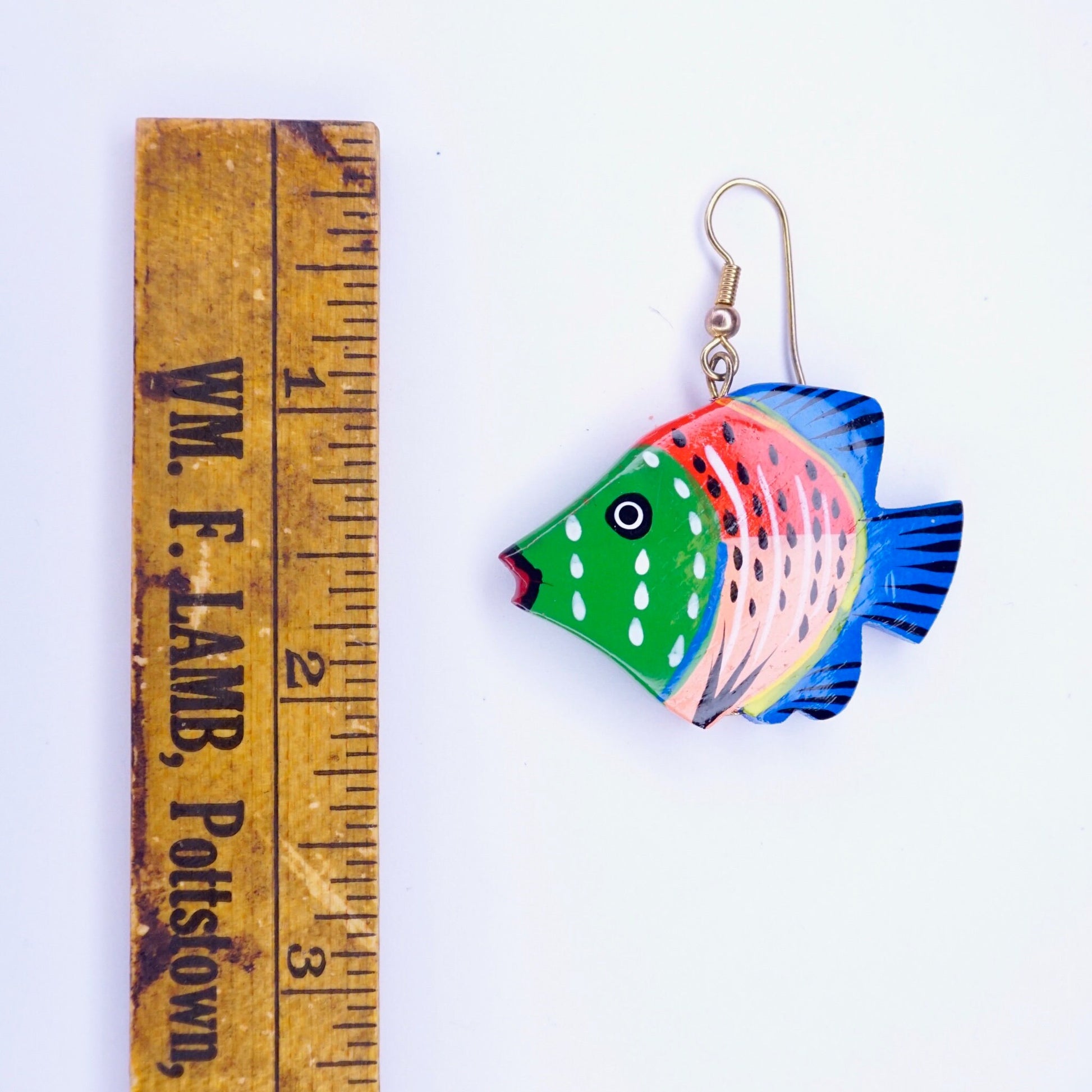 Alt text: Handmade vintage wood carved fish earrings with colorful paint detailing, displayed next to a ruler for scale.