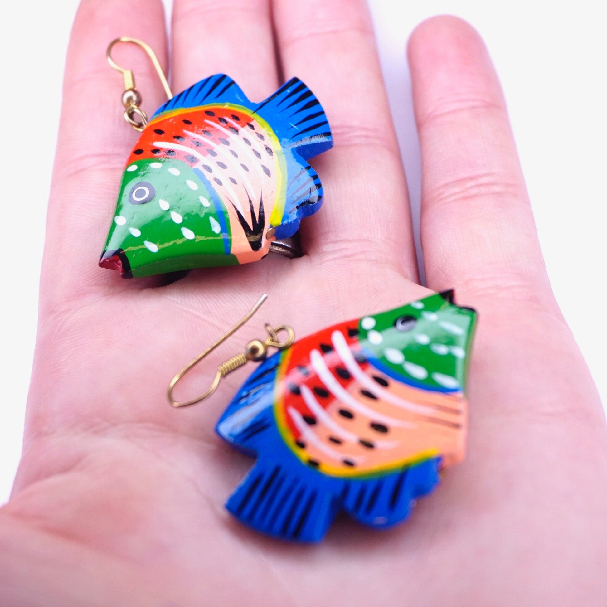 Hand holding vintage colorful carved wood fish dangle earrings with detailed painting, handmade statement wooden jewelry.