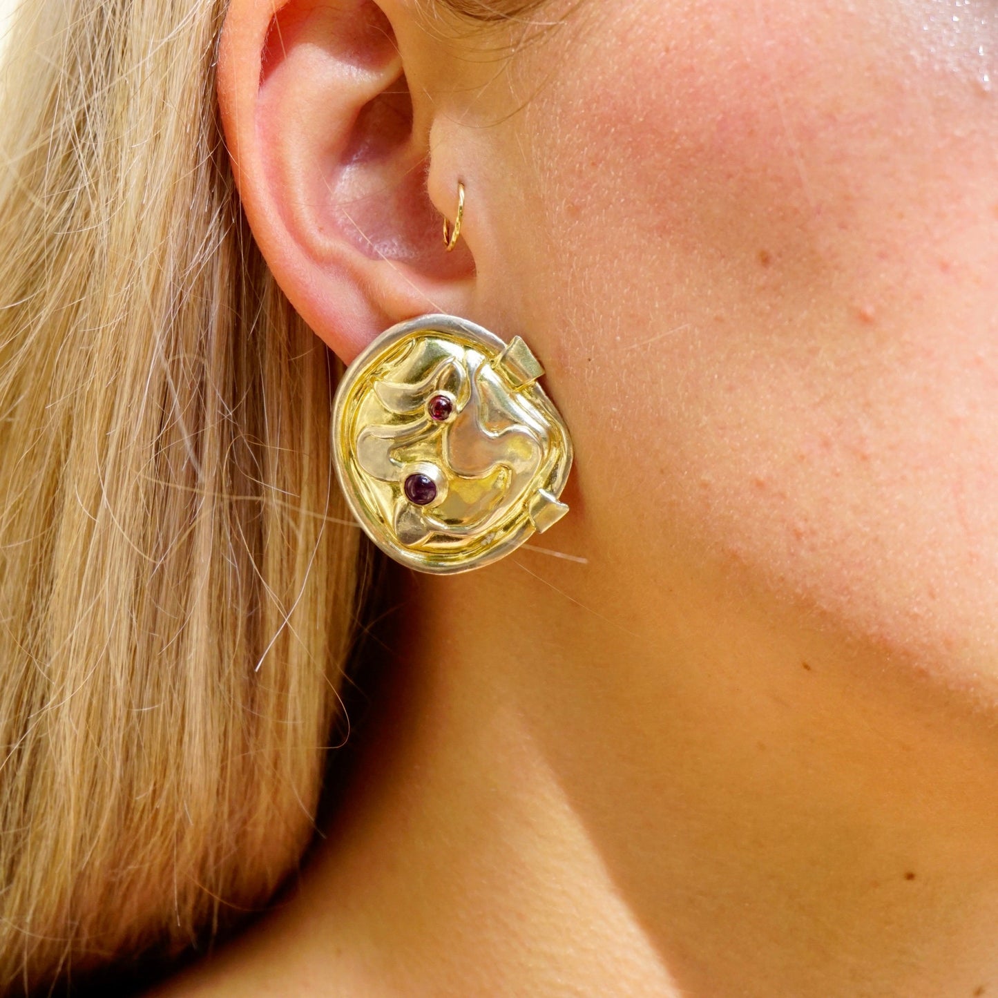 Close-up of a woman's ear wearing a vintage William and Shellie modernist sterling silver earring featuring small amethyst gemstones in an abstract design.