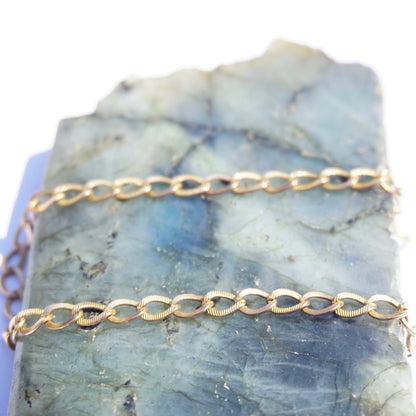 Delicate vintage 10K gold Cuban chain bracelet, 7 inches long, thin minimalist gold links on light blue stone background