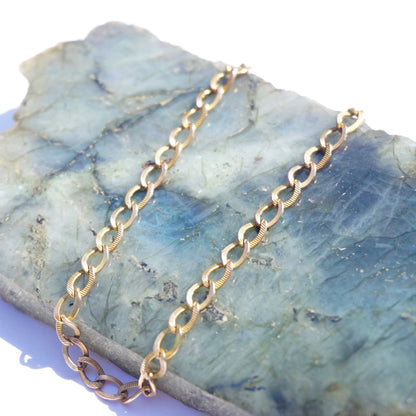 Vintage 10K gold Cuban chain bracelet on blue stone background, featuring a delicate 7-inch minimalist gold chain with thin interlocking links.