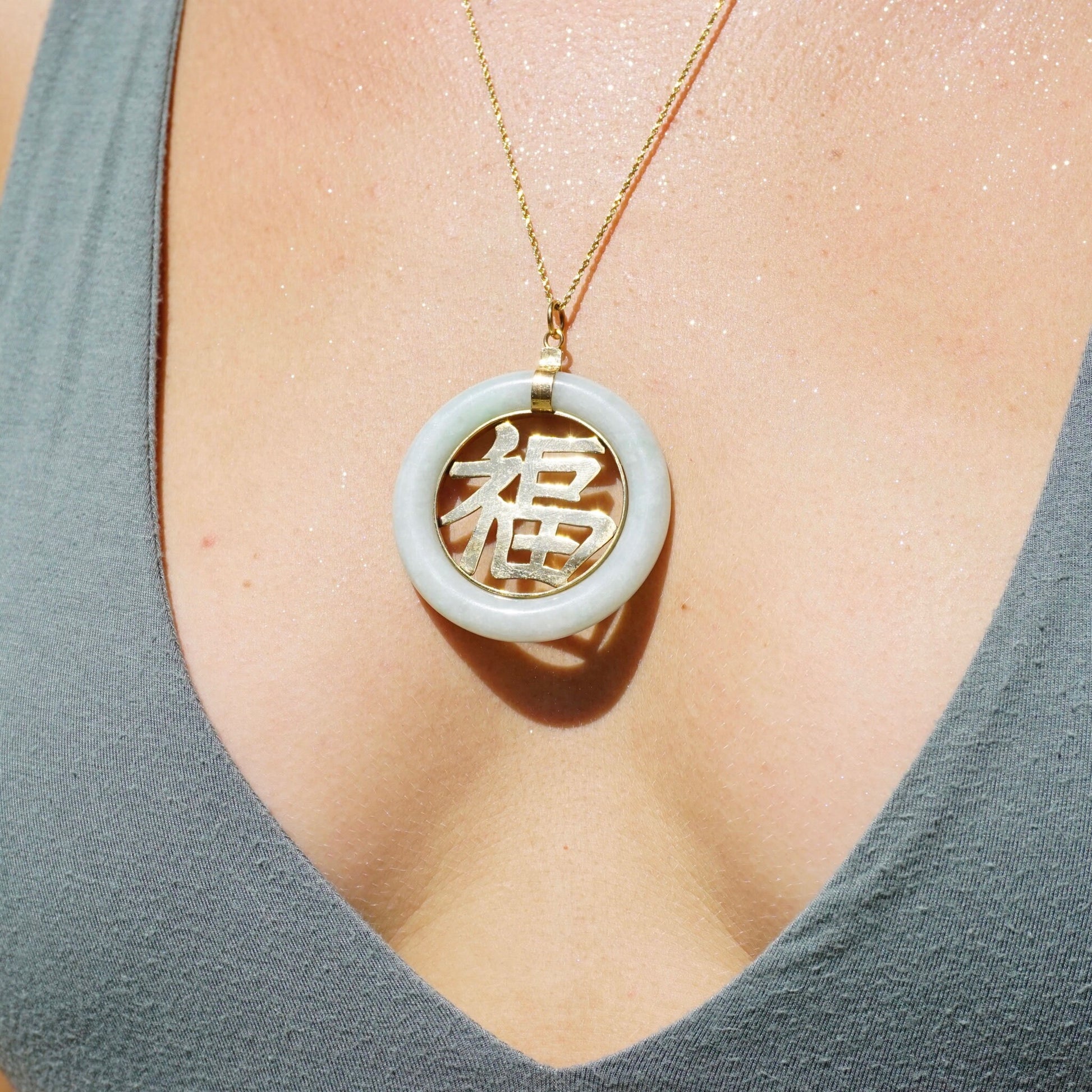 Vintage 14K gold jade Chinese symbol pendant necklace featuring a large, light green jade pendant carved with a Chinese character, suspended from a delicate gold chain against a woman's chest.