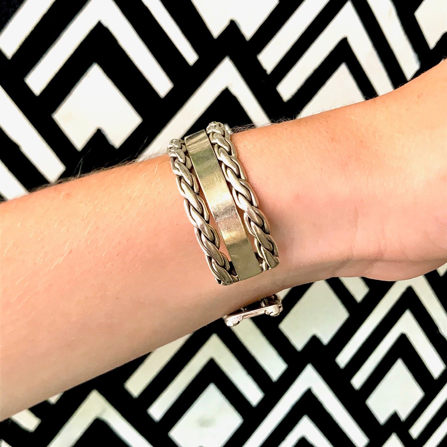 Vintage sterling silver cuff bracelet with woven chain detail on wrist against black and white geometric patterned background