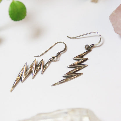 Vintage sterling silver lightning bolt earrings with carved details, minimal dangle style, unique silver drop earrings on white background with green leaves.