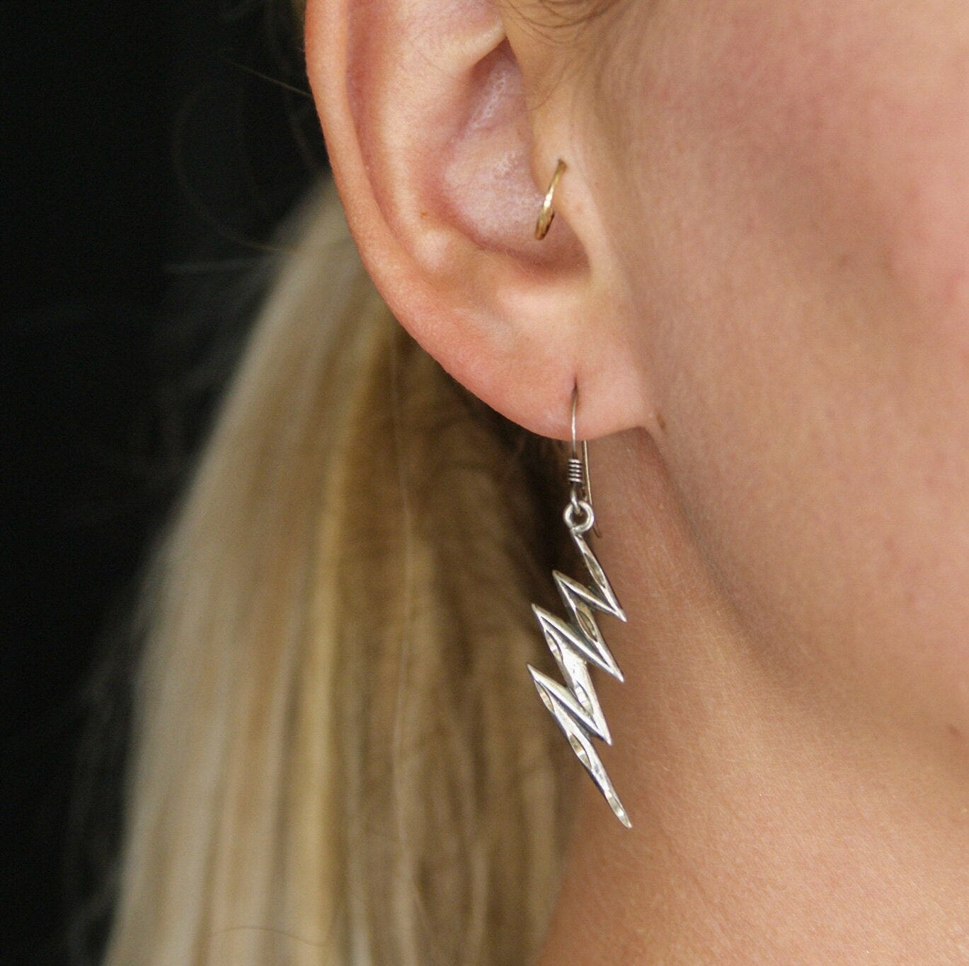 Vintage sterling silver lightning bolt earrings featuring carved details hang from a woman's ear, providing a unique and minimal dangle earring style.