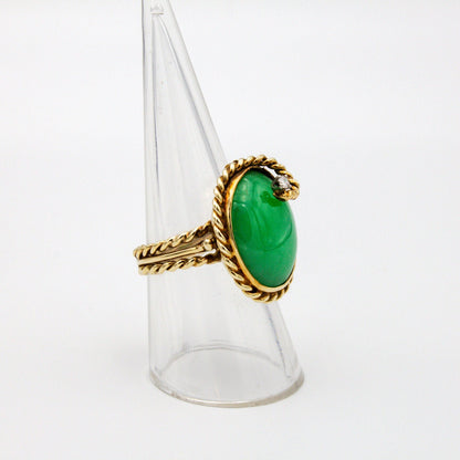 Vintage 14K gold jade and diamond cocktail ring featuring a large oval green jade stone accented by a small diamond, set in a twisting gold band, displayed on a clear ring holder stand.