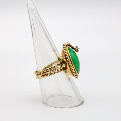 Vintage 14K gold jade and diamond cocktail ring featuring a large green jade stone accented by a twisted gold rope design and a single diamond, set on a clear acrylic ring display stand against a plain white background.