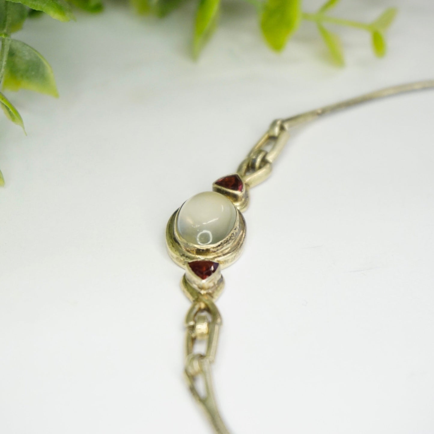 Vintage sterling silver choker necklace with moonstone pendant and red gemstone accents against a blurred green foliage background.