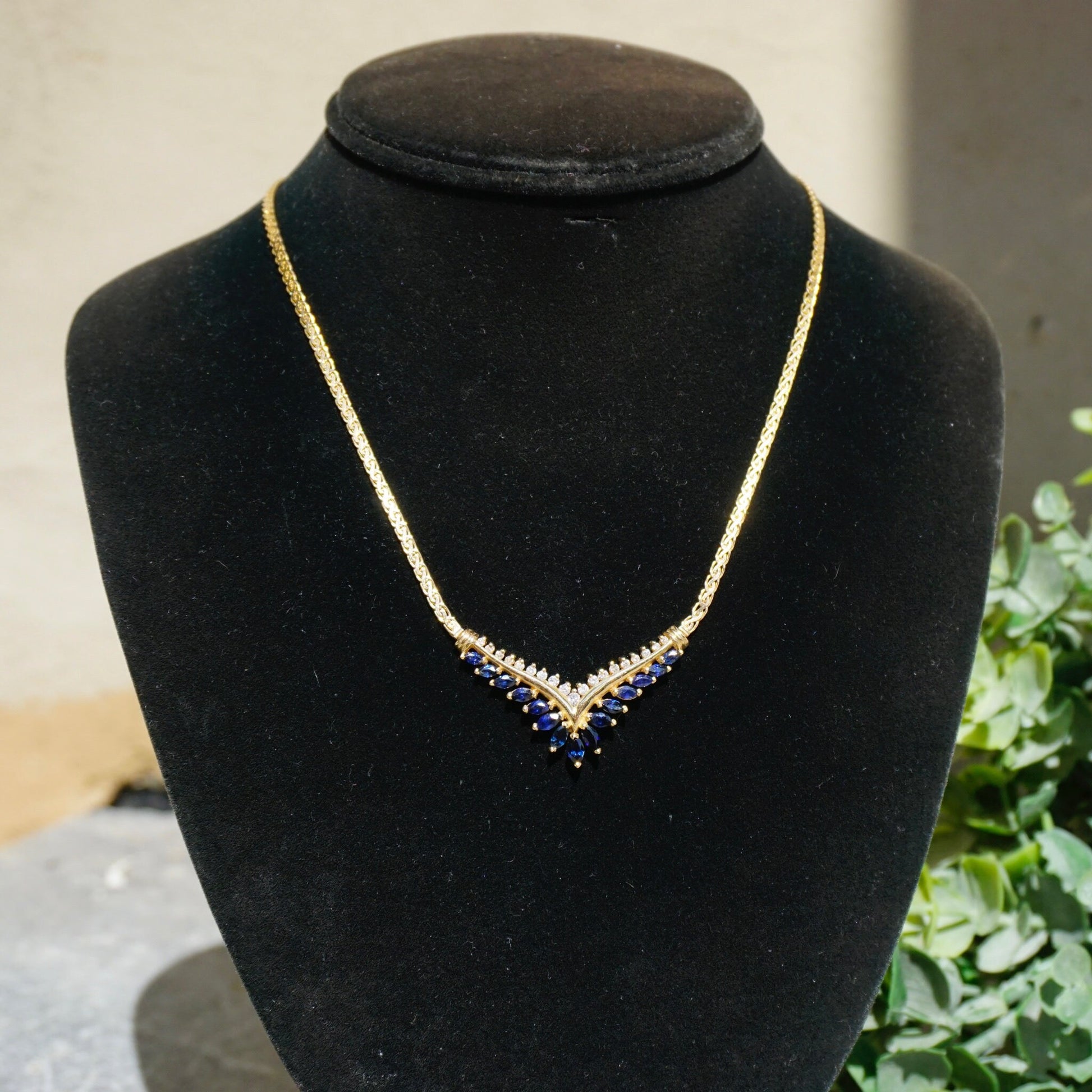 Elegant vintage 14k gold choker necklace with sapphire and diamond stones, forming a V-shaped pendant design on a thin gold chain, displayed on a black velvet jewelry stand.