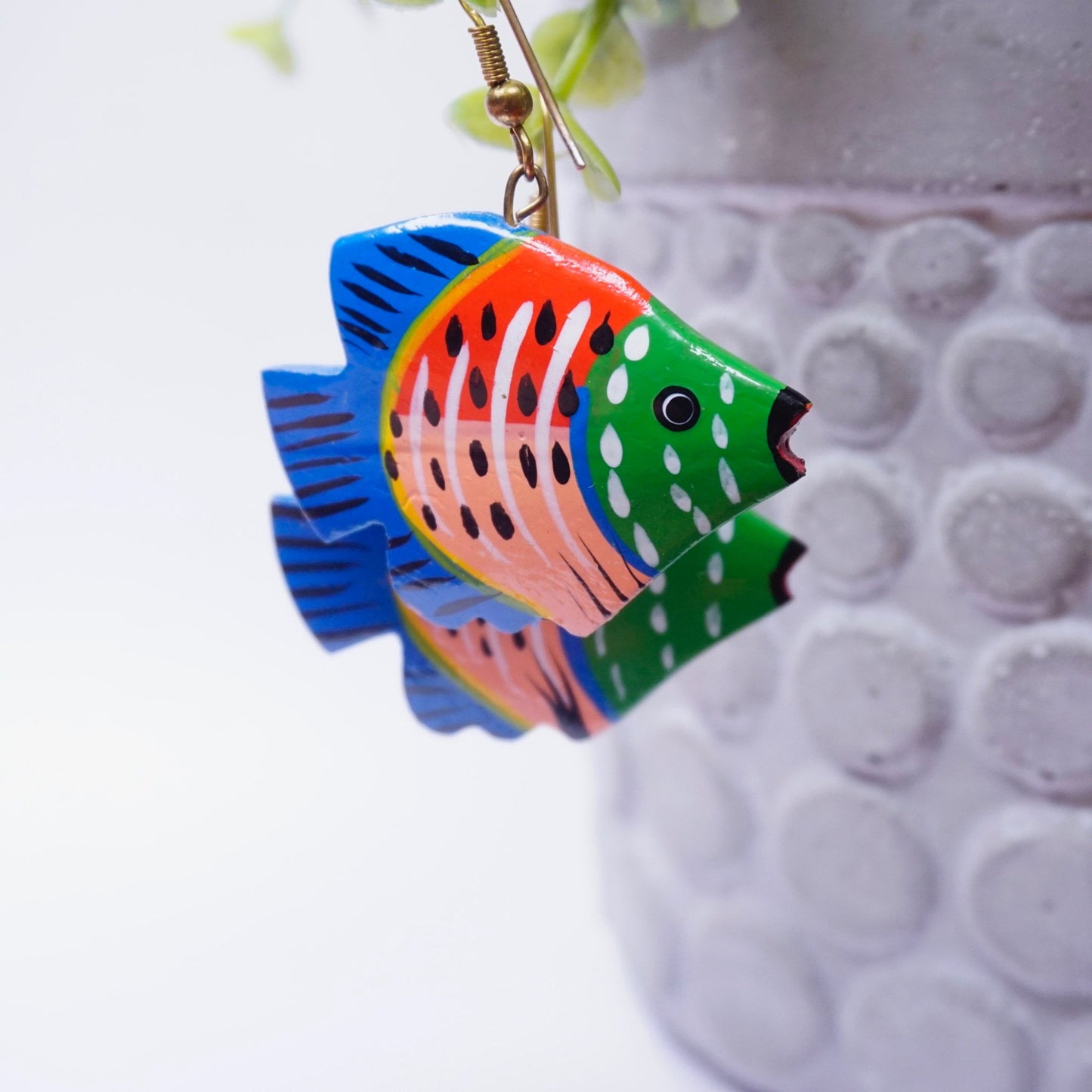 Handmade vintage colorful wood carved fish dangle earrings with detailed painting suspended against blurred background.