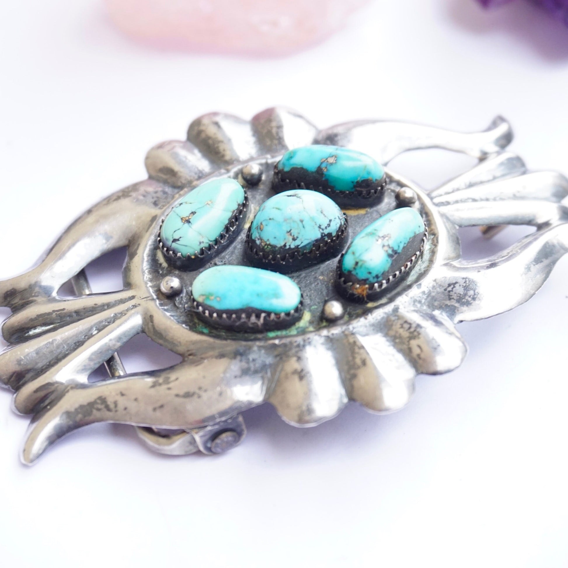 Vintage Navajo sterling silver belt buckle featuring multiple vibrant turquoise stones in various shapes and sizes, set in an intricate silver design resembling a sunburst or floral motif, with the blue stones providing striking contrast against the oxidized silver. An exquisite example of Native American craftsmanship and old pawn silver jewelry.