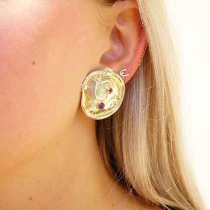 Vintage gold-tone sterling silver abstract modernist earrings with small amethyst gemstones, shown on a woman's ear against her blond hair.