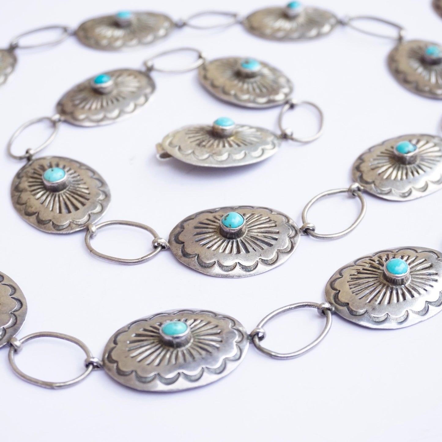 Vintage Native American sterling silver concho belt with turquoise accents, featuring intricately stamped silver oval conchos linked by silver rings, each concho set with a small round turquoise stone at the center, creating an adjustable statement piece of Southwest jewelry.