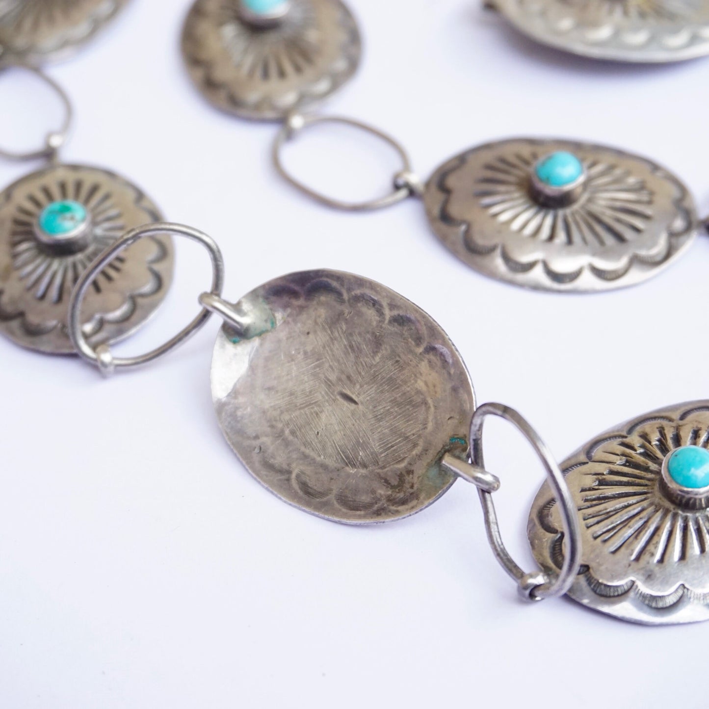 Vintage Native American sterling silver concho belt with turquoise accents. Adjustable silver belt features round concho designs each set with a small turquoise stone in the center. Close-up view of the silver conchos and turquoise stones against a white background. An example of traditional Old Pawn Native American jewelry craftsmanship.