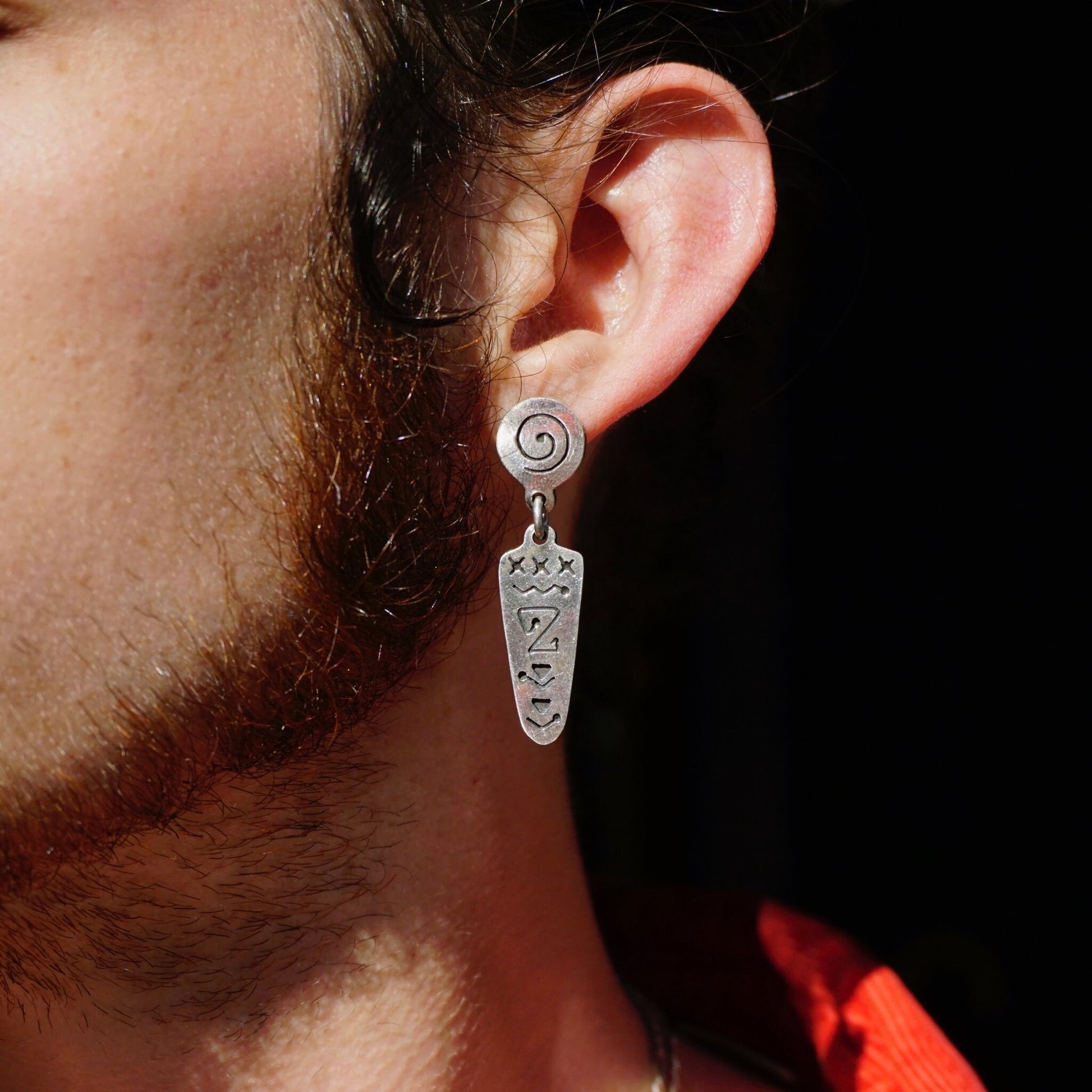 Alt text: Close-up of an ear wearing a unique vintage sterling silver dangle earring with an abstract swirl design, set against a black background.