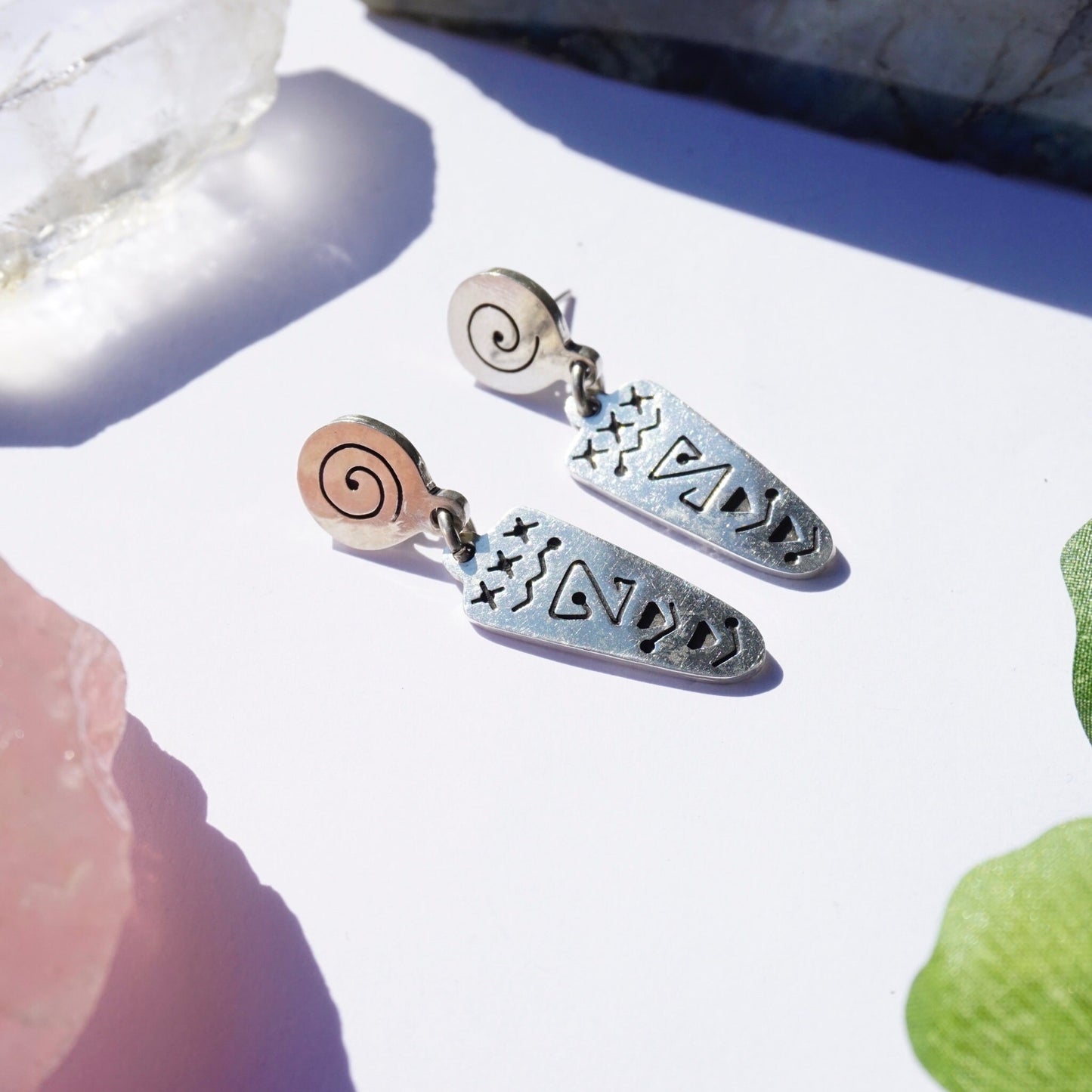 Vintage sterling silver dangle stud earrings with unique abstract swirl design against a white background with pink and green foliage accents.