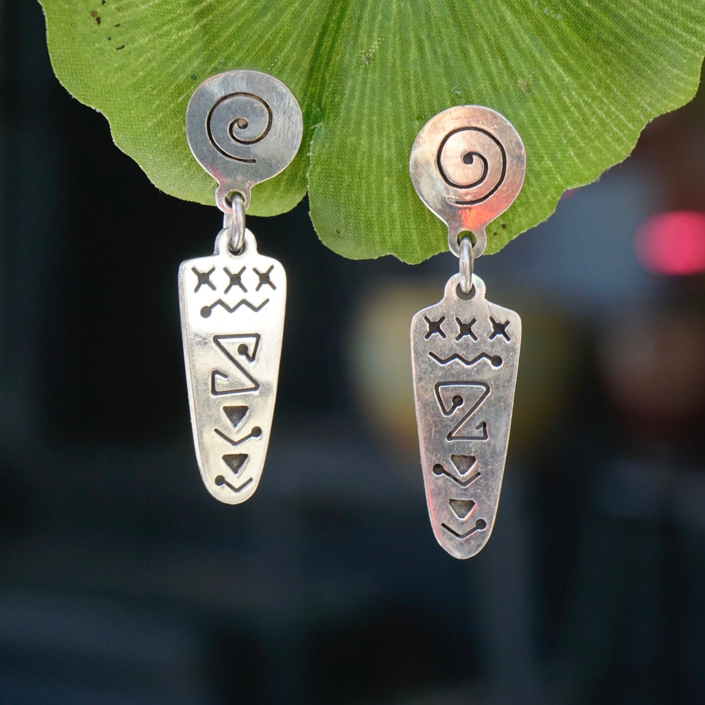 Vintage sterling silver abstract dangle earrings with unique swirl design, displayed on a green leaf background.