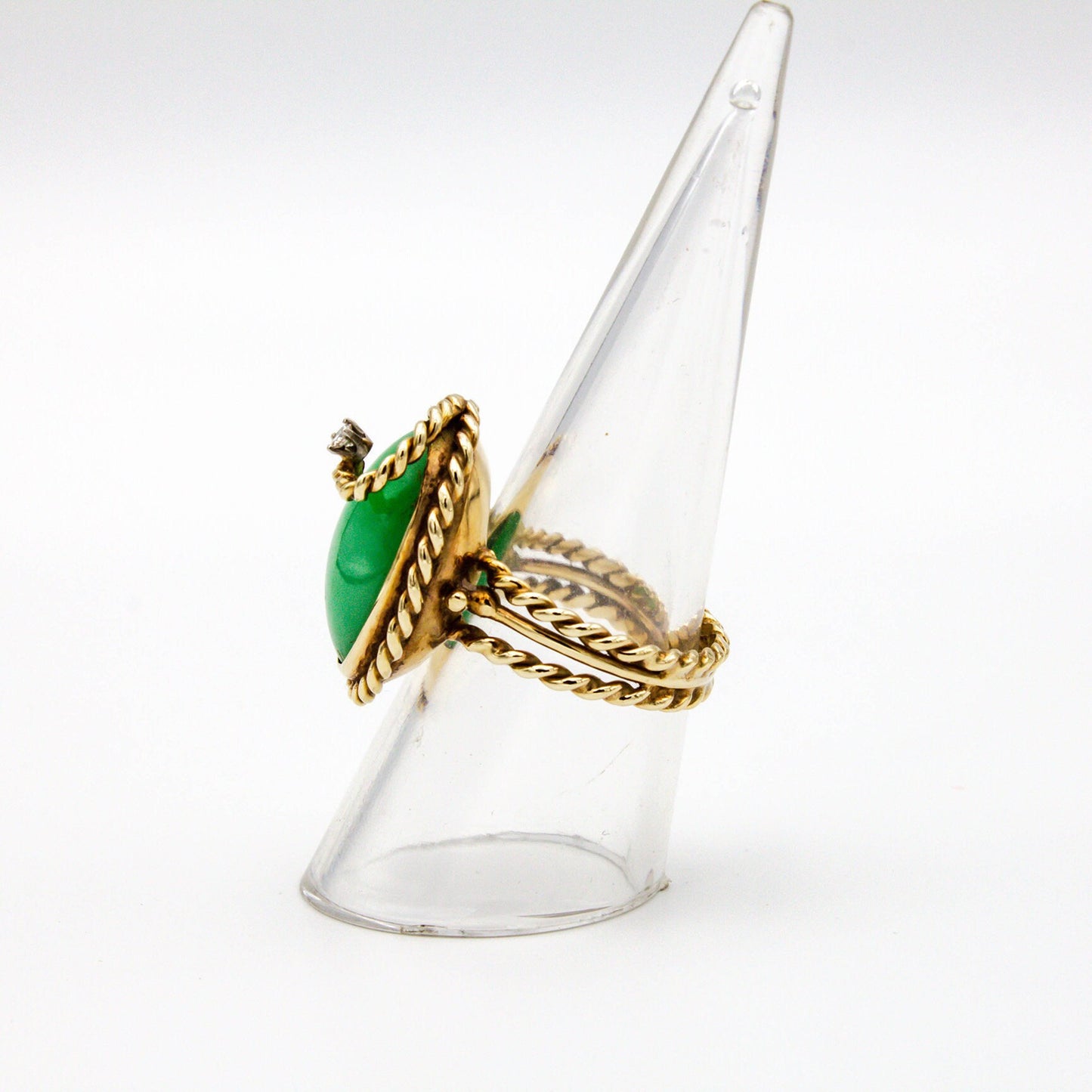 Vintage 14K gold cocktail ring featuring a large green jade stone accented by a twisted gold band and a small diamond, displayed on a clear plastic ring stand against a white background.