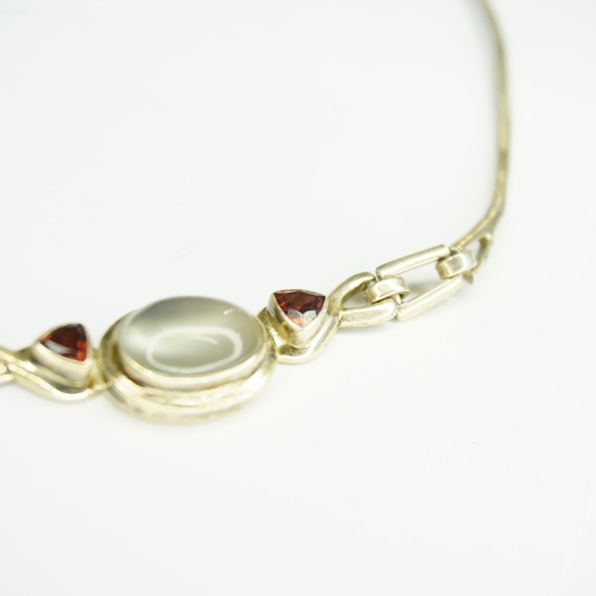 Vintage sterling silver choker necklace featuring a large oval moonstone pendant flanked by two small round red gemstones, set on a delicate silver chain against a white background.