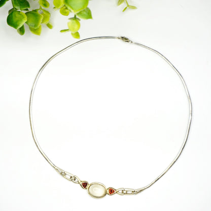 Vintage sterling silver choker necklace with moonstone pendant and red jewel accents on a white background with green leaves