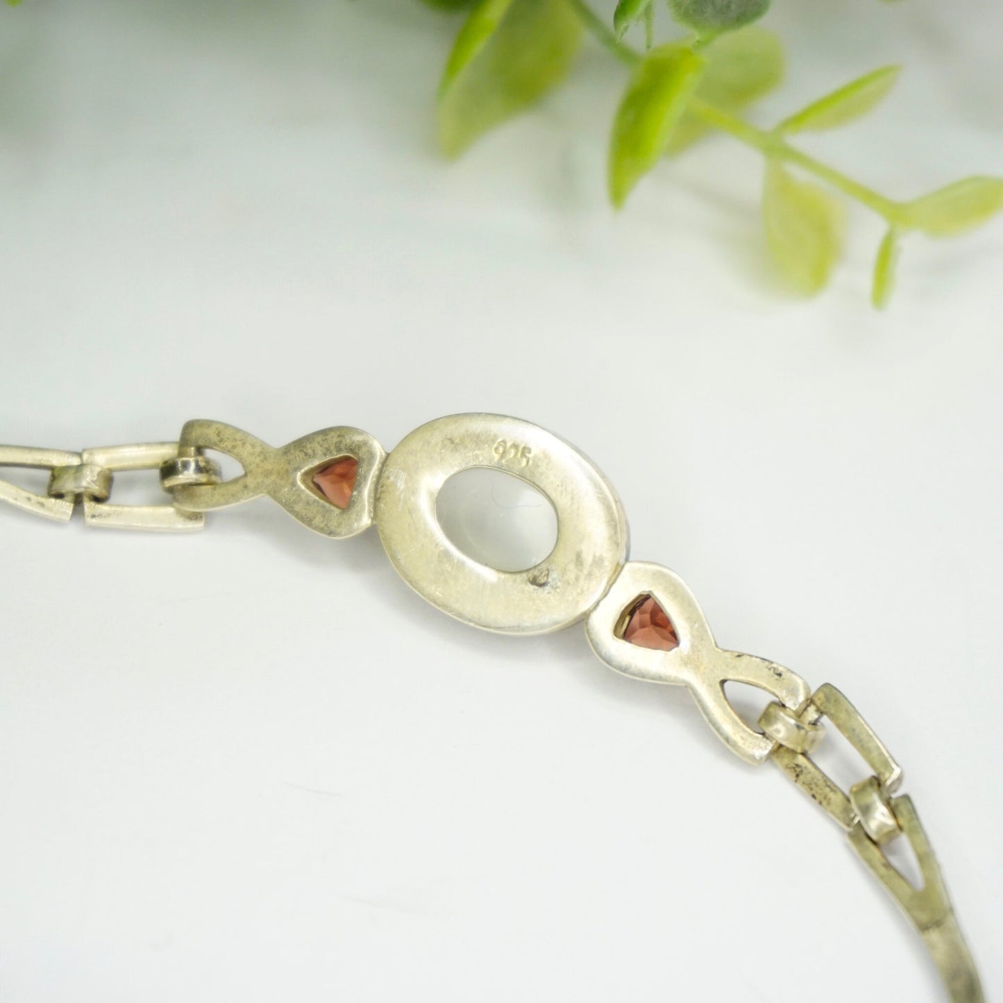 Vintage sterling silver moonstone choker necklace with red jewel accents on a silver chain, displayed with green leaves in the background.