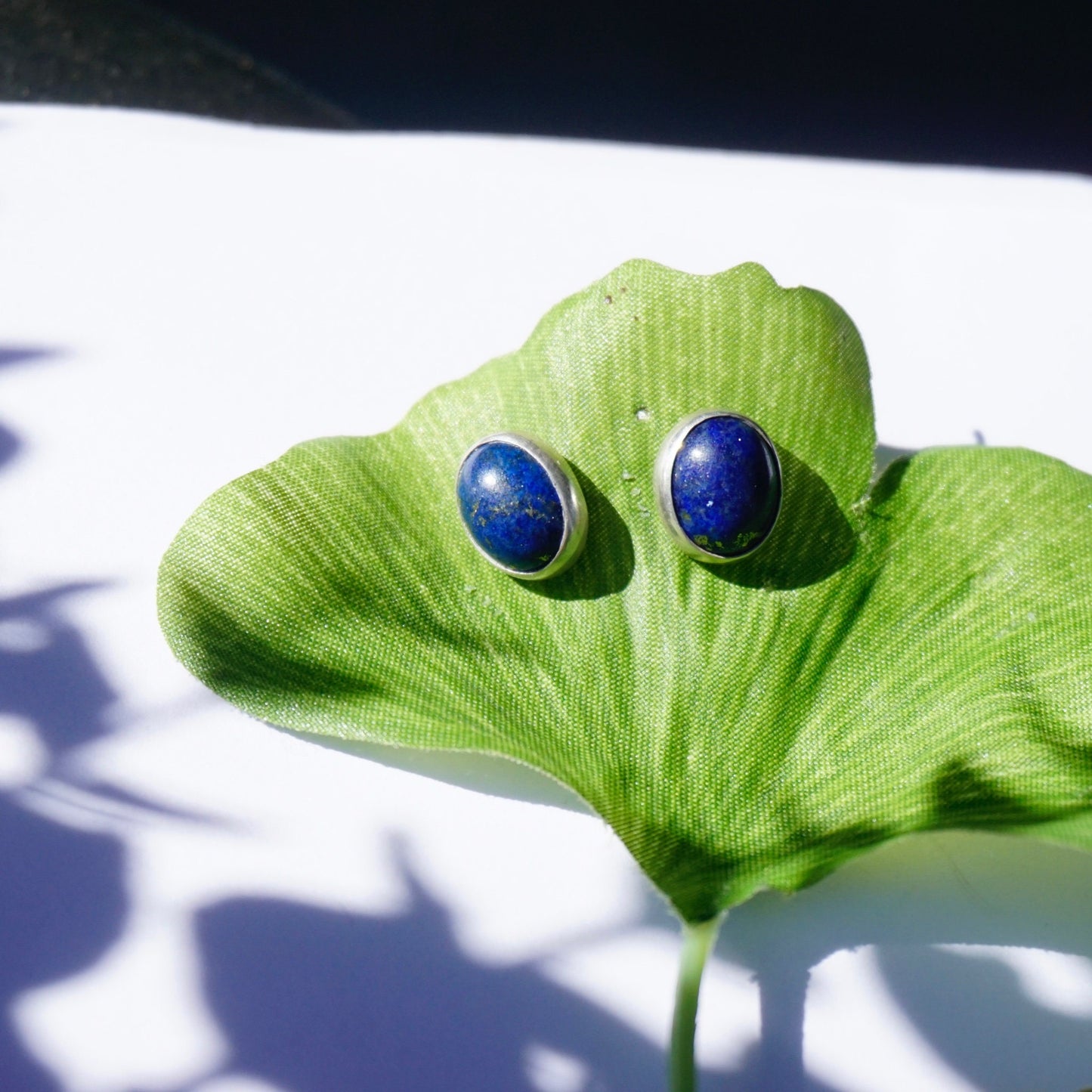 Green leaf with two blue lapis lazuli stone stud earrings against white background