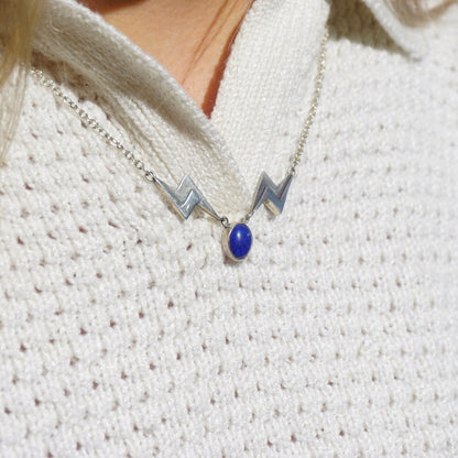 Vintage lapis lazuli and silver lightning bolt pendant necklace on a silver chain, shown on a white knit sweater.