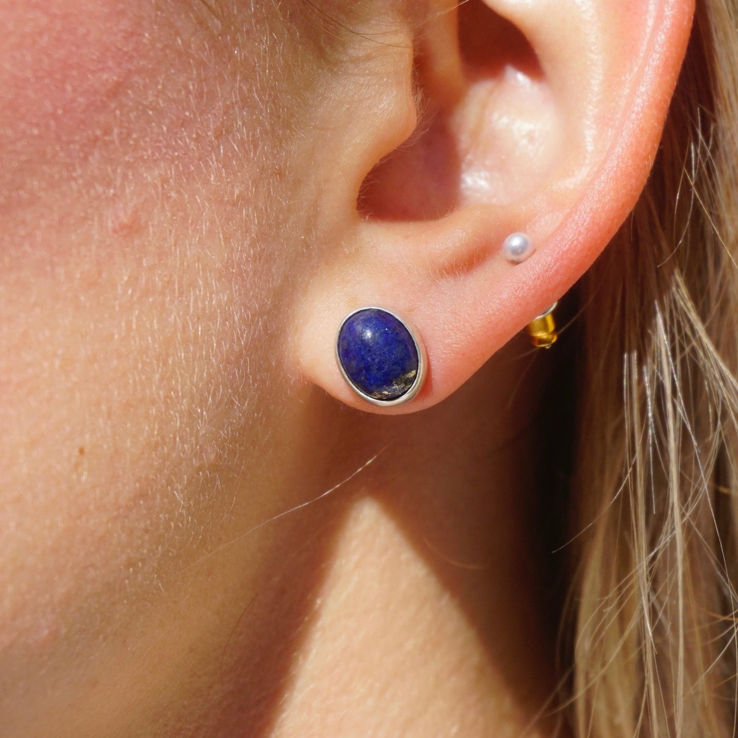 Close-up photo of an ear wearing a minimalist lapis lazuli stud earring set in sterling silver against bare skin.