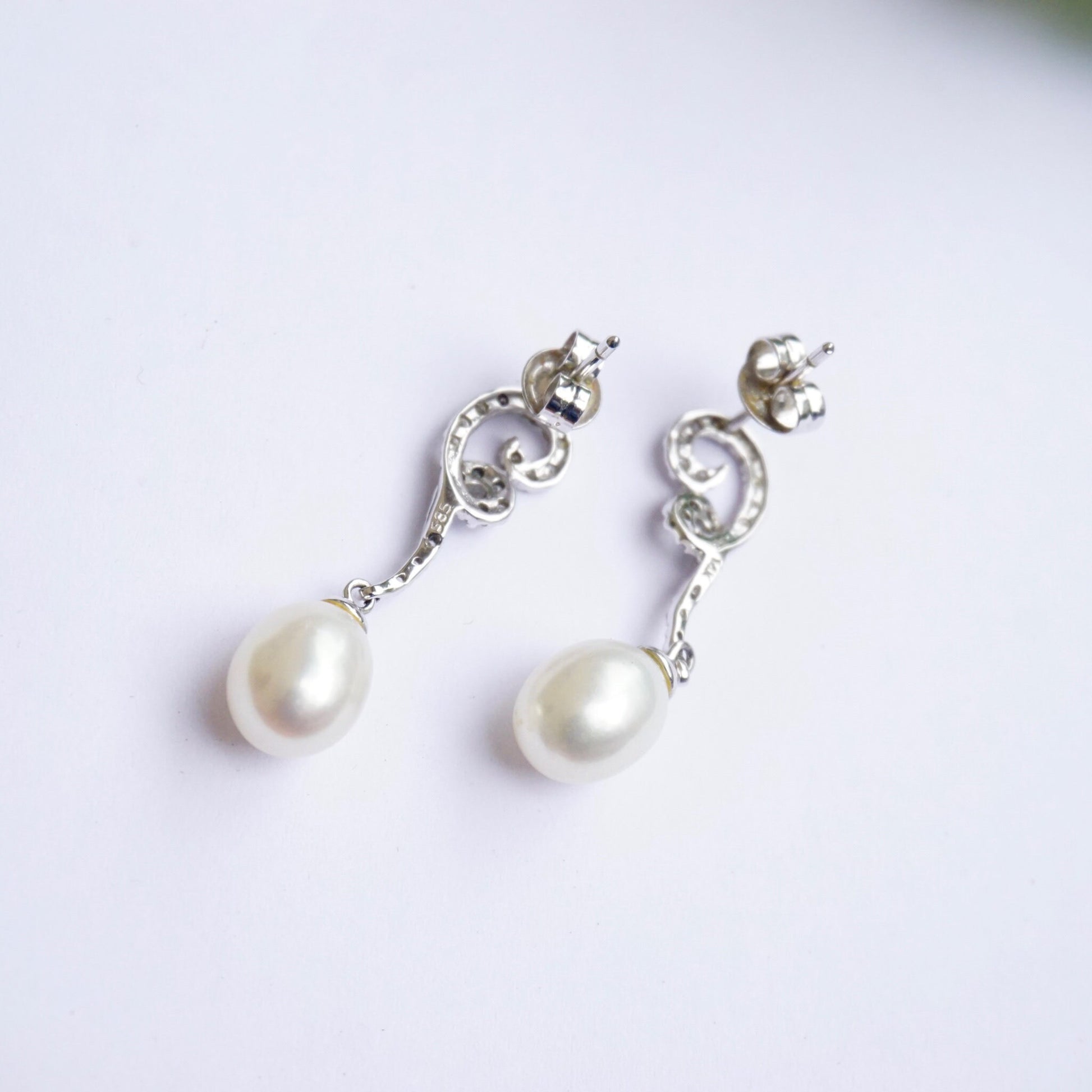 Vintage 14K white gold diamond and pearl drop earrings featuring delicate pearl drops suspended from ornate diamond-accented studs, displayed on a white background.