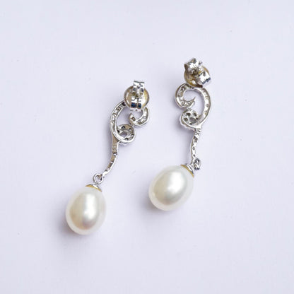 Vintage 14K white gold diamond and pearl drop earrings featuring delicate pearl drops suspended from diamond-accented swirling posts, an elegant and timeless fine jewelry accessory.