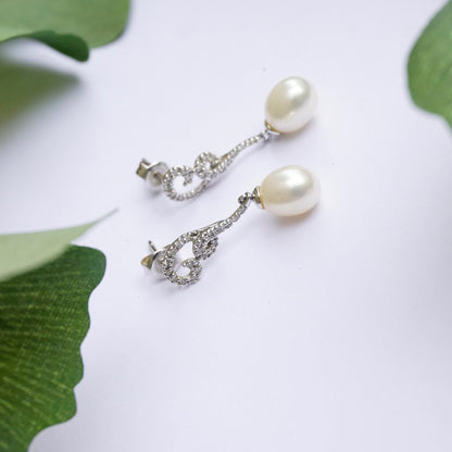 Vintage 14K white gold pearl and diamond drop earrings featuring delicate teardrop pearls suspended from sparkling diamond-accented posts, an elegant and timeless fine jewelry accessory.